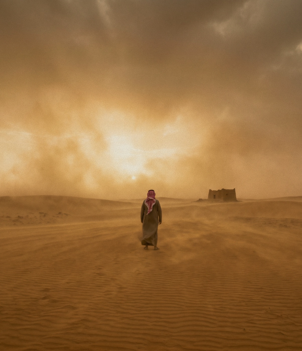 شخصٌ بالزيّ التقليدي يعبر الصحراء نحو أطلالٍ تراثية